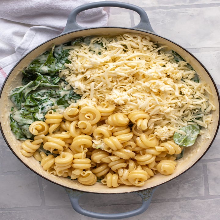 Pasta, cheese, and spinach in a pot for mac 'n' cheese.