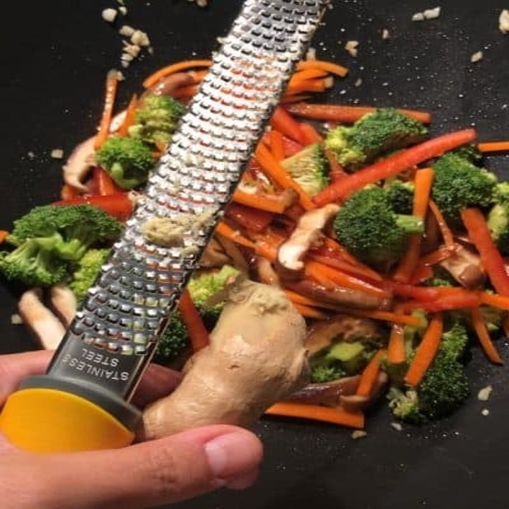Grating ginger into sautéed vegetables.