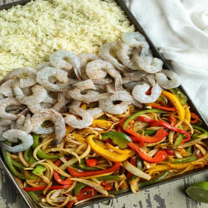 Shrimp, cauliflower rice, onions, and peppers on a sheet pan.