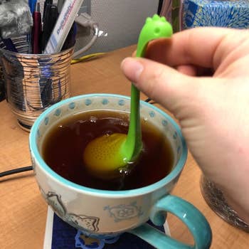 different reviewer's photo of the green dino submerged in a mug of tea
