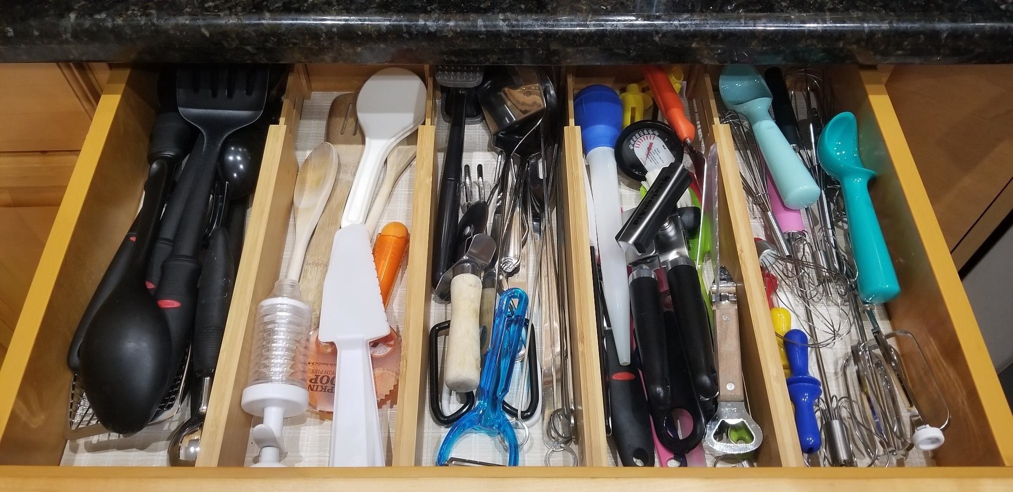 A reviewer photo of an open drawer with four drawer dividers inside organizing a slew of various kitchen utensils 