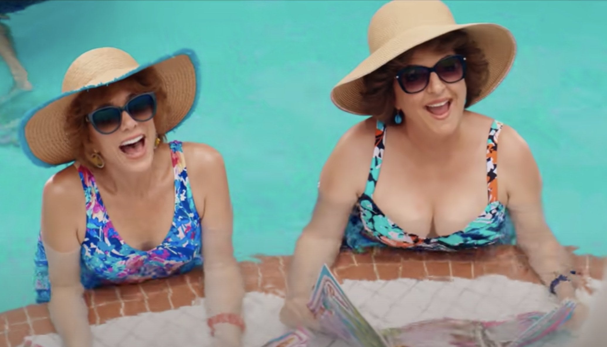 Barb and Star sit in a pool in multi colored bathing suits and large straw hats