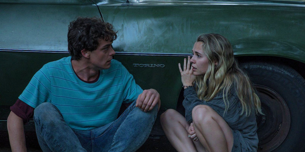 Caleb (Israel Broussard) and Rain crouching down on the ground while leaning against the side of a car in Fear Of Rain 