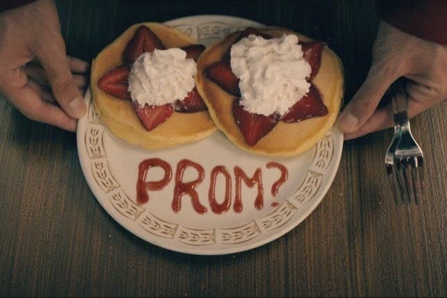 A stack of pancakes and "prom?" question written in strawberry syrup
