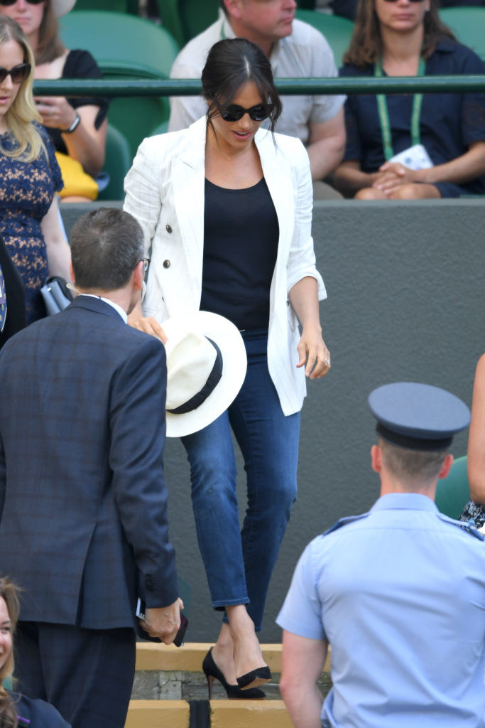 Meghan walking down stairs, wearing sunglasses, jeans, a white jacket, and high heels