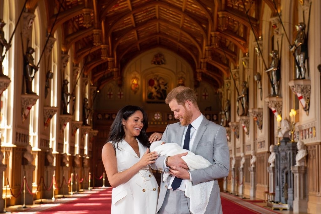 Meghan wears a white trench dress while she and Harry pose with baby Archie