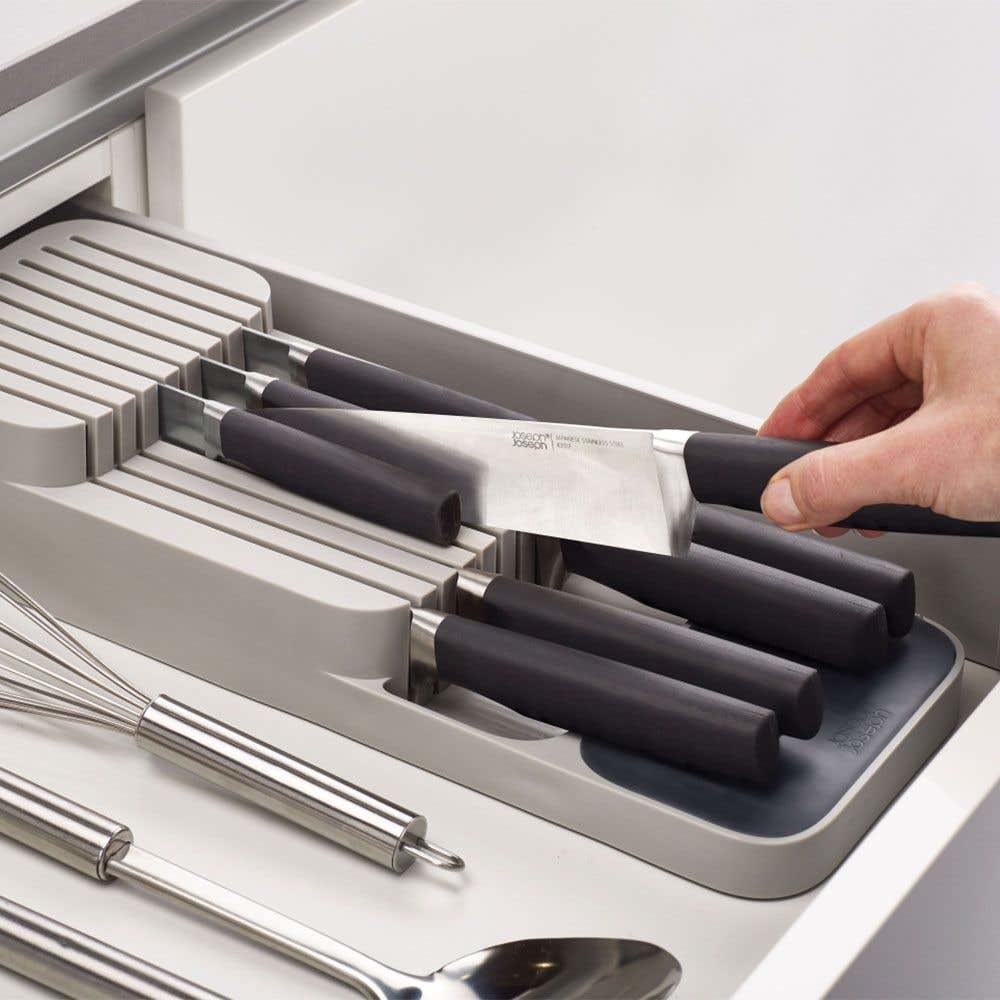 A person picking up a knife from its sleeve of a mat with knives organized neatly 