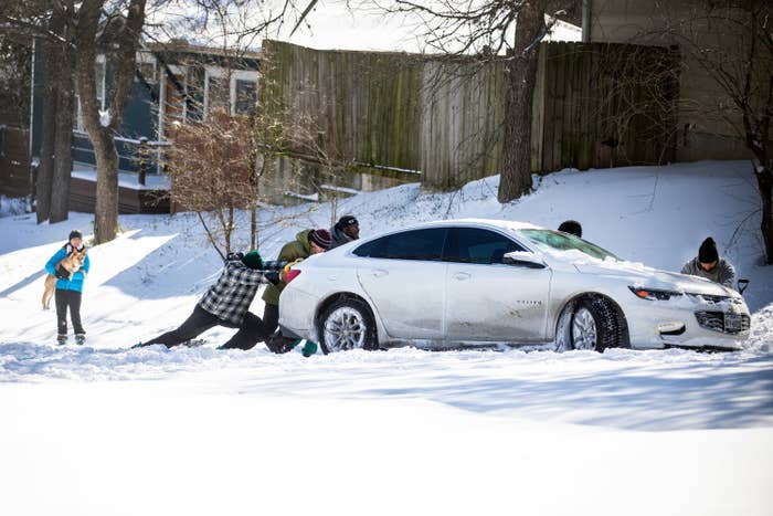 Several people try to push a car through the snow in front of a house