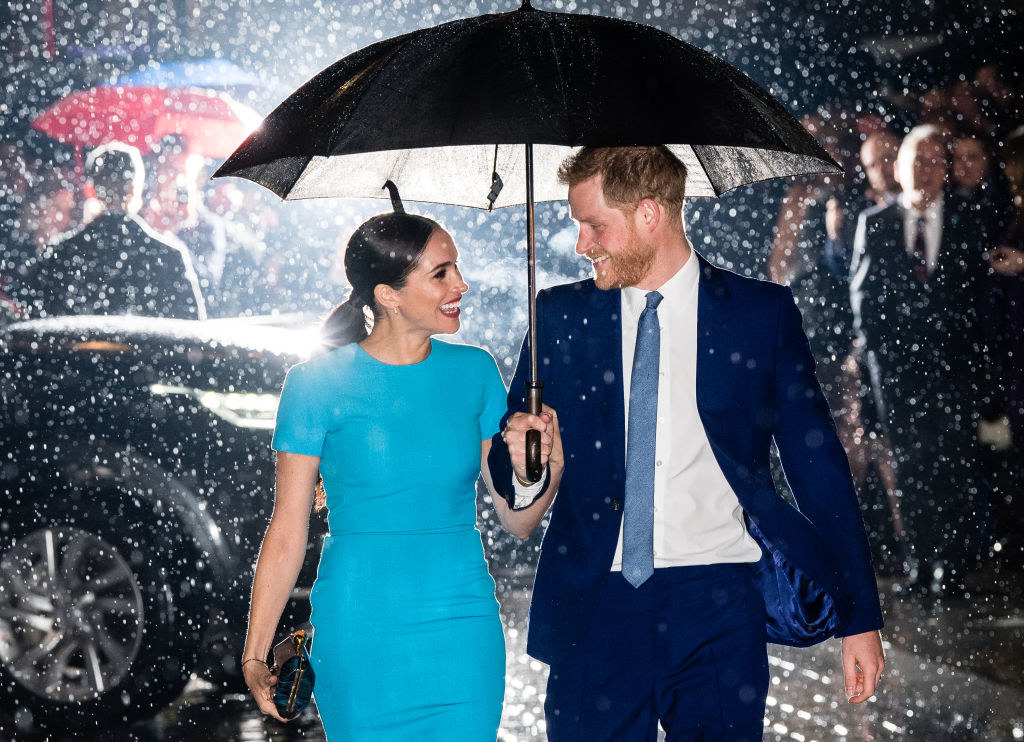 Meghan and Harry smile at each other and walk under an umbrella in the rain