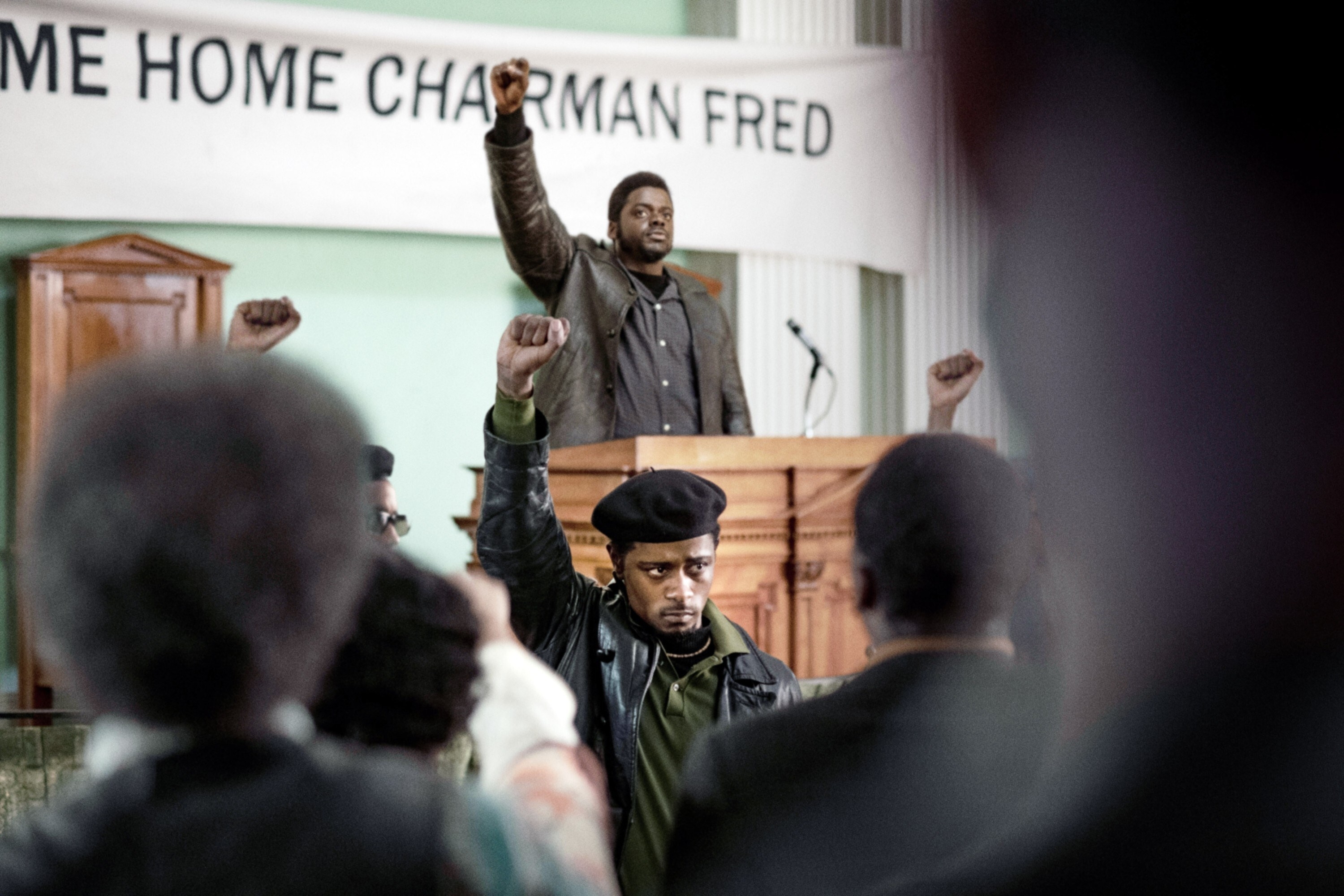 LaKeith Stanfield as William O&#x27;Neal raises his fist in the air, mirroring the same pose as Daniel Kaluuya as Fred Hampton, who is standing on a stage behind him