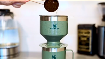 a person pouring coffee into the top of the green metal pour over