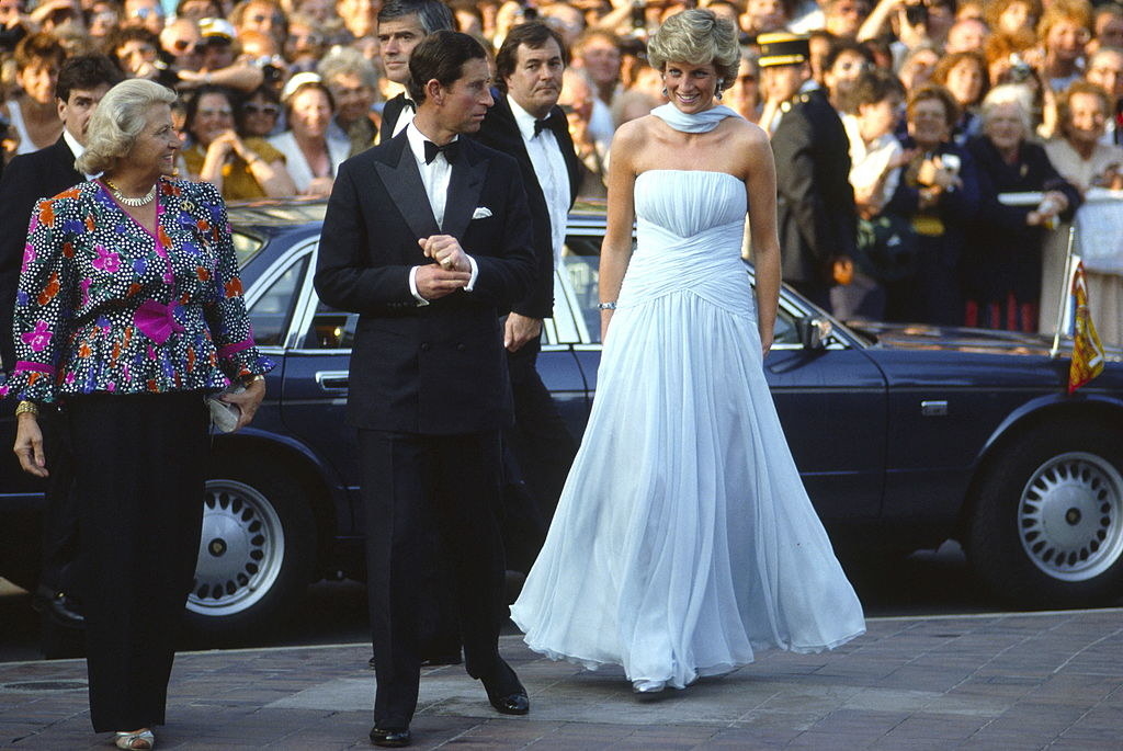 Princess Diana wearing a strapless, long white gown and walking alongside Prince Charles