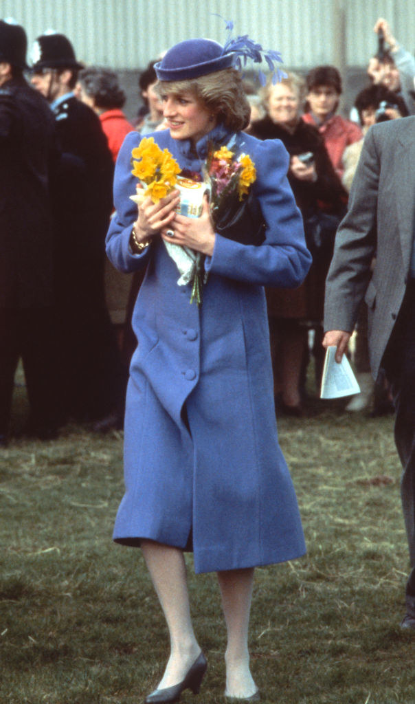 Diana wears a long, puffy coat and a hat with silk flowers