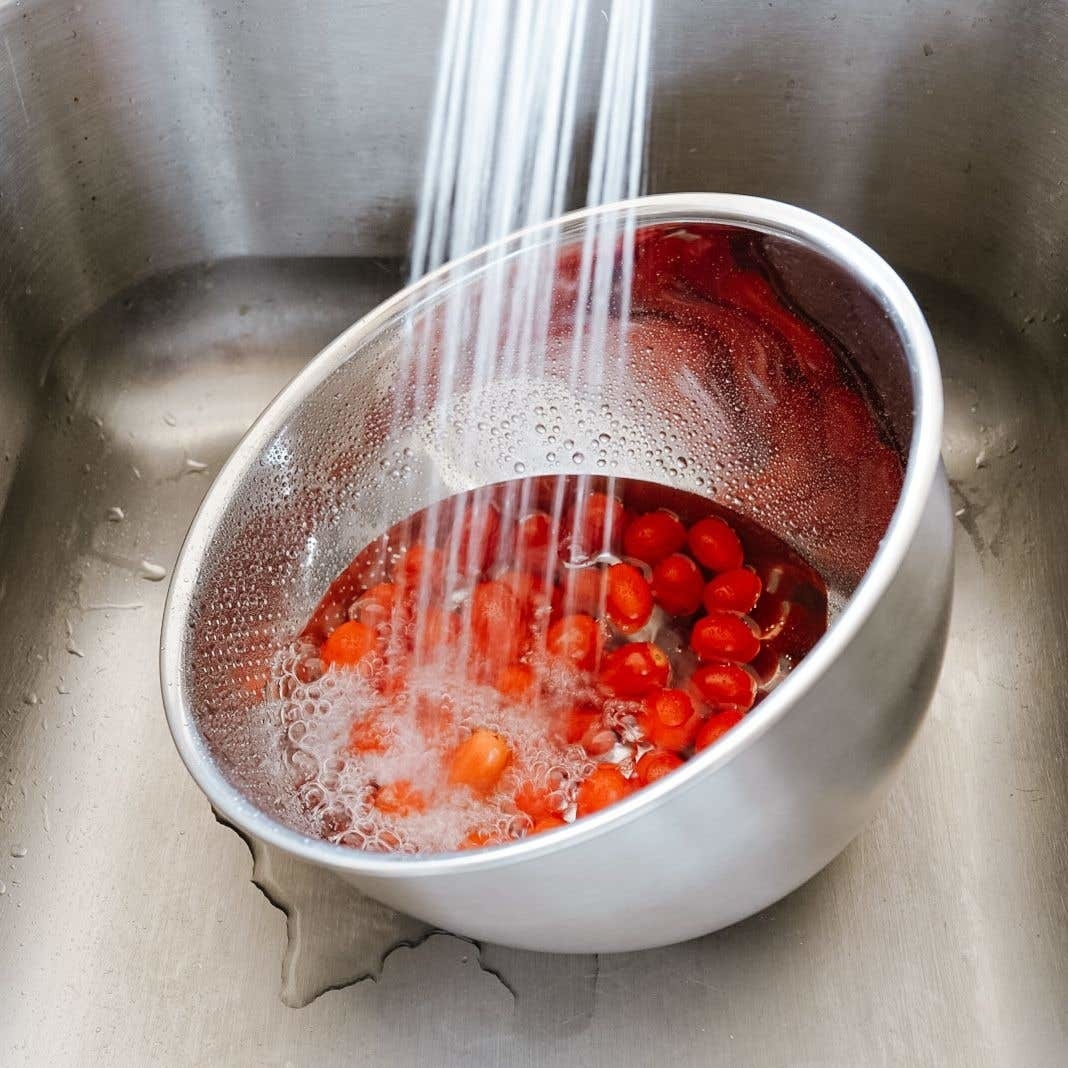 A large bowl filled with grape tomatoes and water that has perforated side 