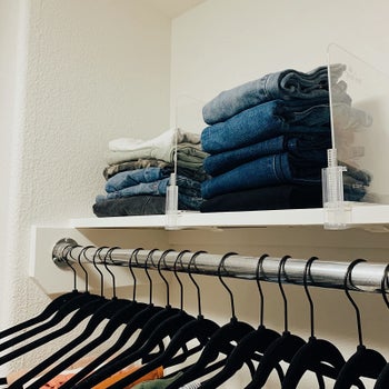reviewer image of two acrylic shelf dividers keeping two stacks of folded pants and jeans organized 