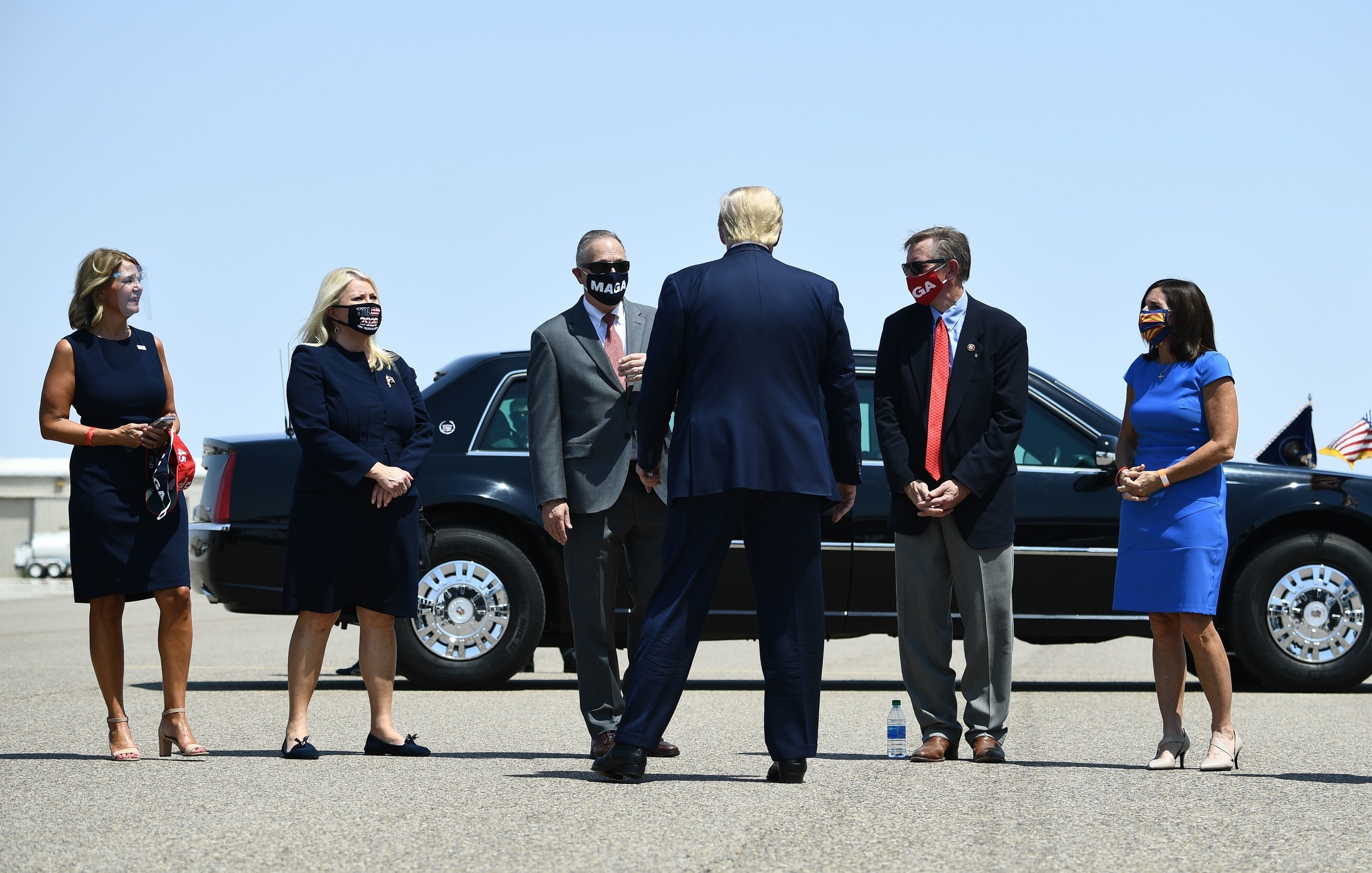 Five members of Congress stand on the tarmac in front of Trump, who has his back to the camera