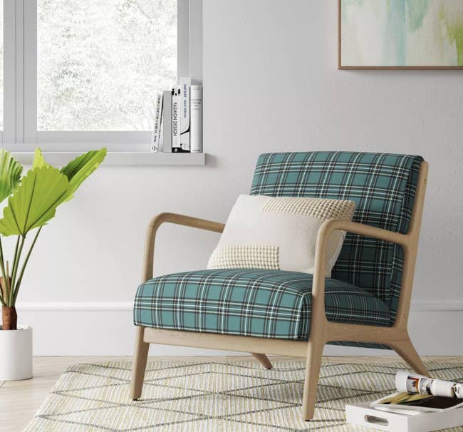 a green black and white plaid upholstered armchair with light wood arms and legs, sitting in a corner