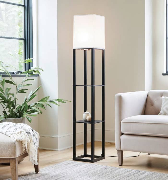 a floor lamp with a white cube lampshade and two black metal shelves