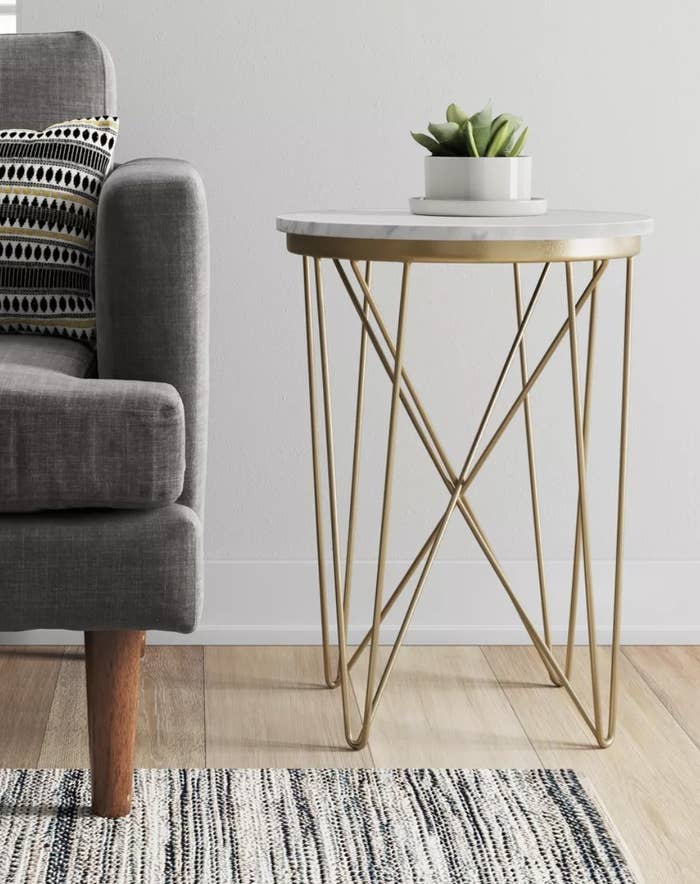 a marble top end table with brass legs next to a couch