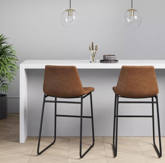 two faux brown leather bar stools with backs and black metal legs, at a counter