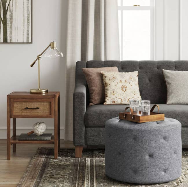 a round grey tufted ottoman in front of a couch, acting as a coffee table