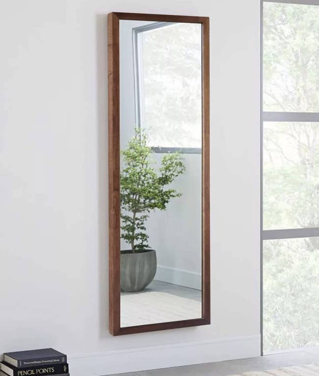 a fulll length mirror with a brown wooden frame hanging on a wall