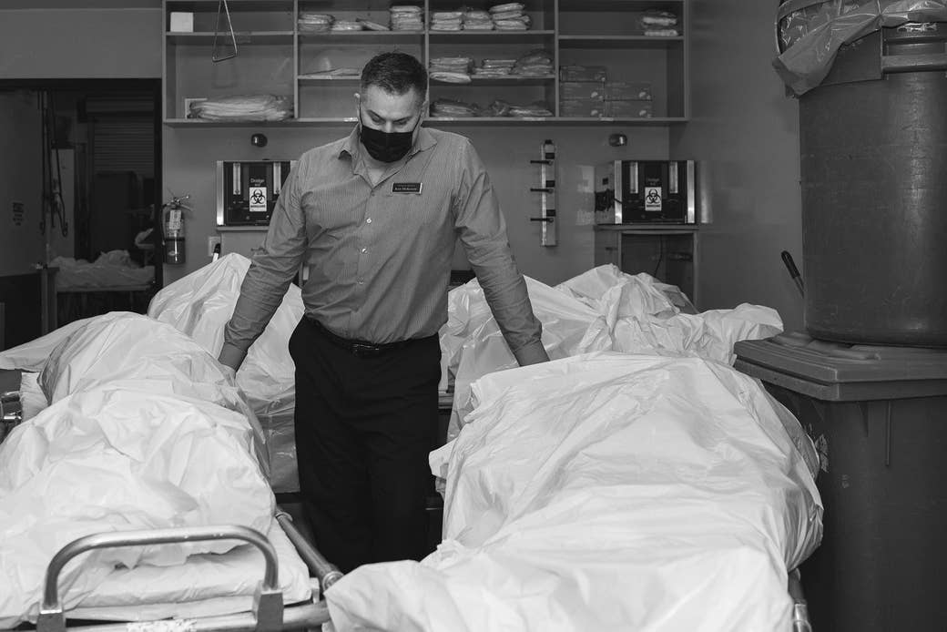 A man stands with a mask on surrounded by bodies in body bags