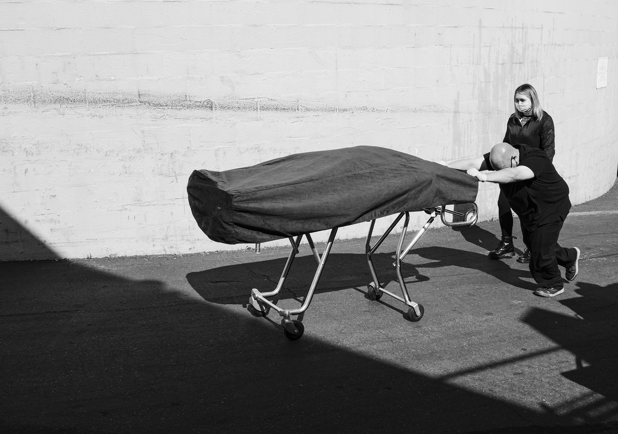 A man pushes a body covered by a cloth on a gurney with a woman next to him