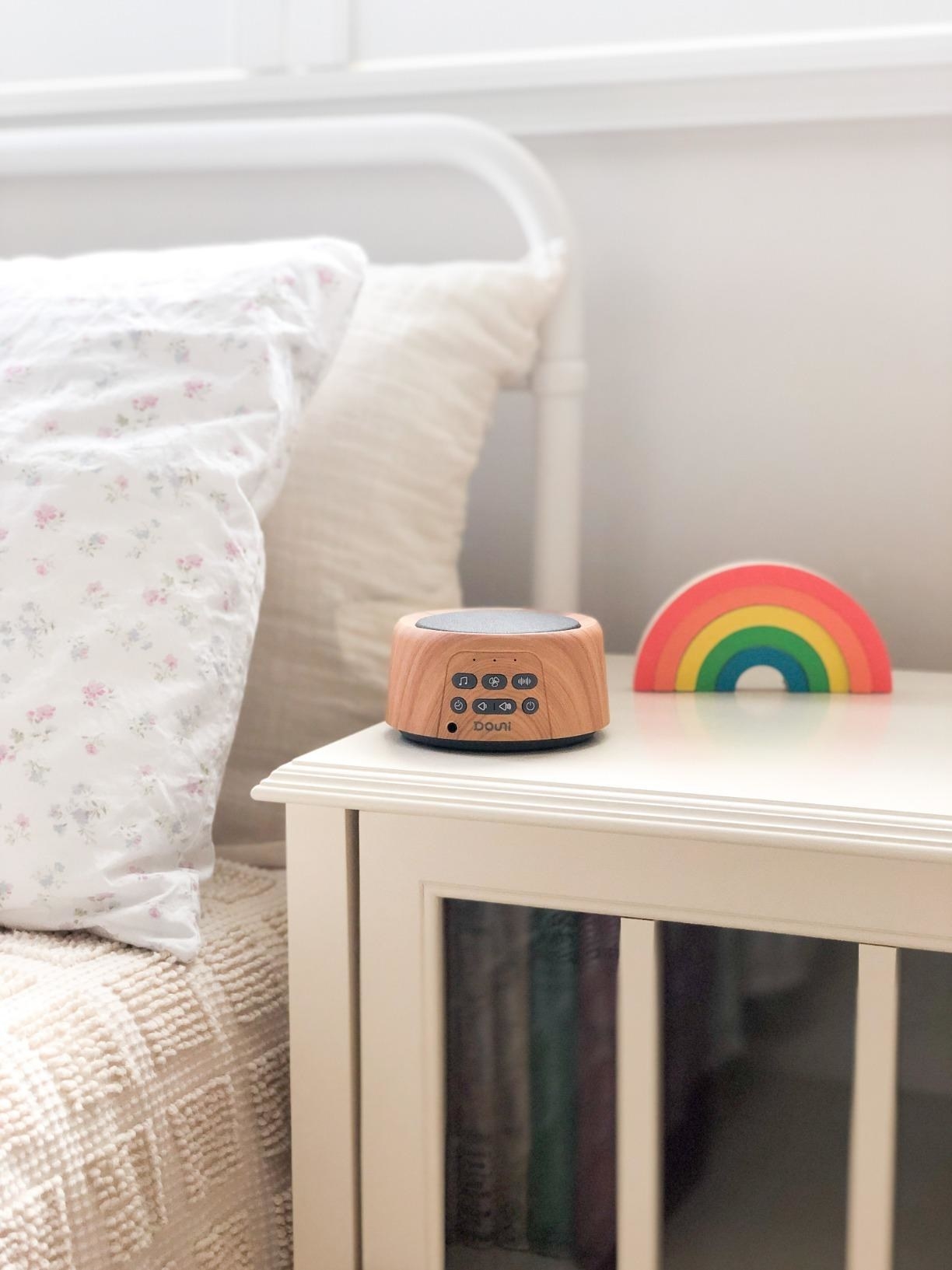 wooden white noise machine on wooden nightstand next to bed