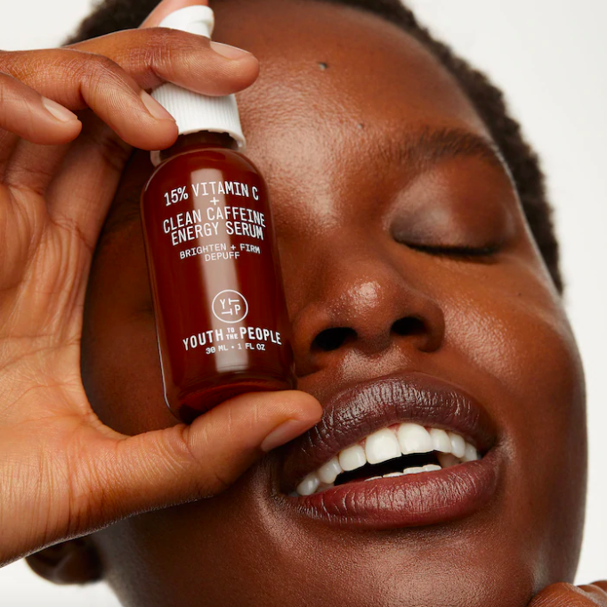 A smiling person holding up the serum to their face