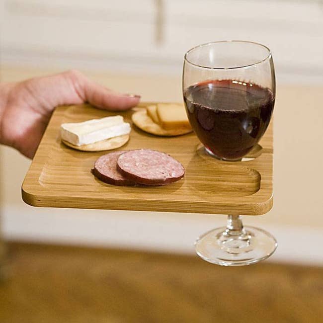 A model holding an individual light wood cheese plate with a small hole a wine glass can rest in 