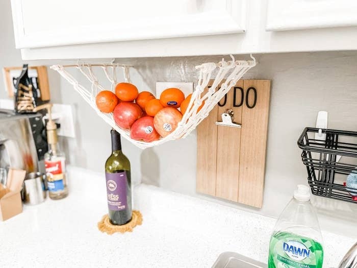 white macrame fruit hammock with oranges and apples above a small kitchen counter