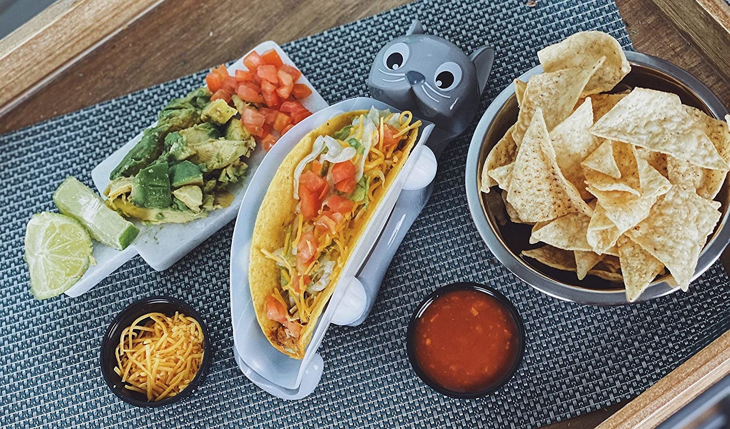 Clear taco holder with a base shaped like a cat laying on it's back. The legs hold up the plastic container.