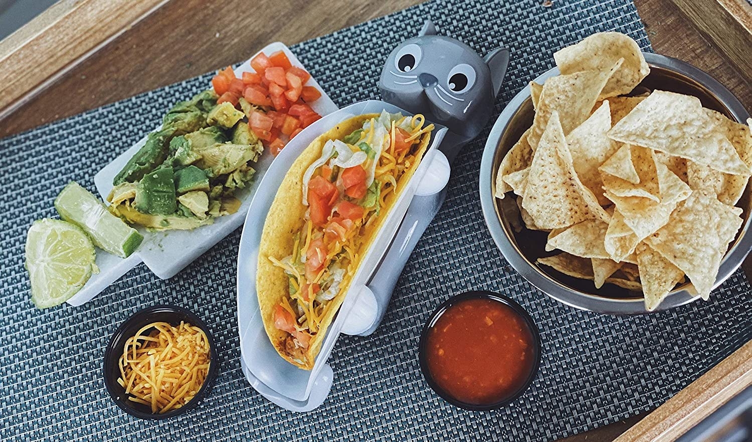 Clear taco holder with a base shaped like a cat laying on it&#x27;s back. The legs hold up the plastic container. 