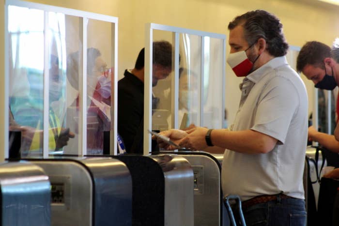 Ted Cruz, wearing a face mask with the Texas flag, checks in at an airport in front of a plexiglass shield