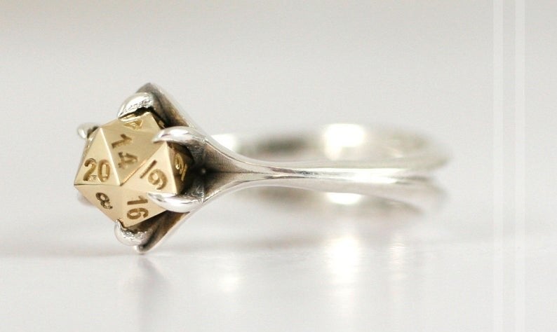 A silver band with a gold center shaped to look like a D20 dice 