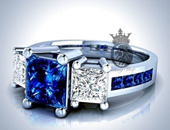 A ring with a center blue sapphire flanked by two square white diamonds and a band encrusted with smaller. blue sapphires 
