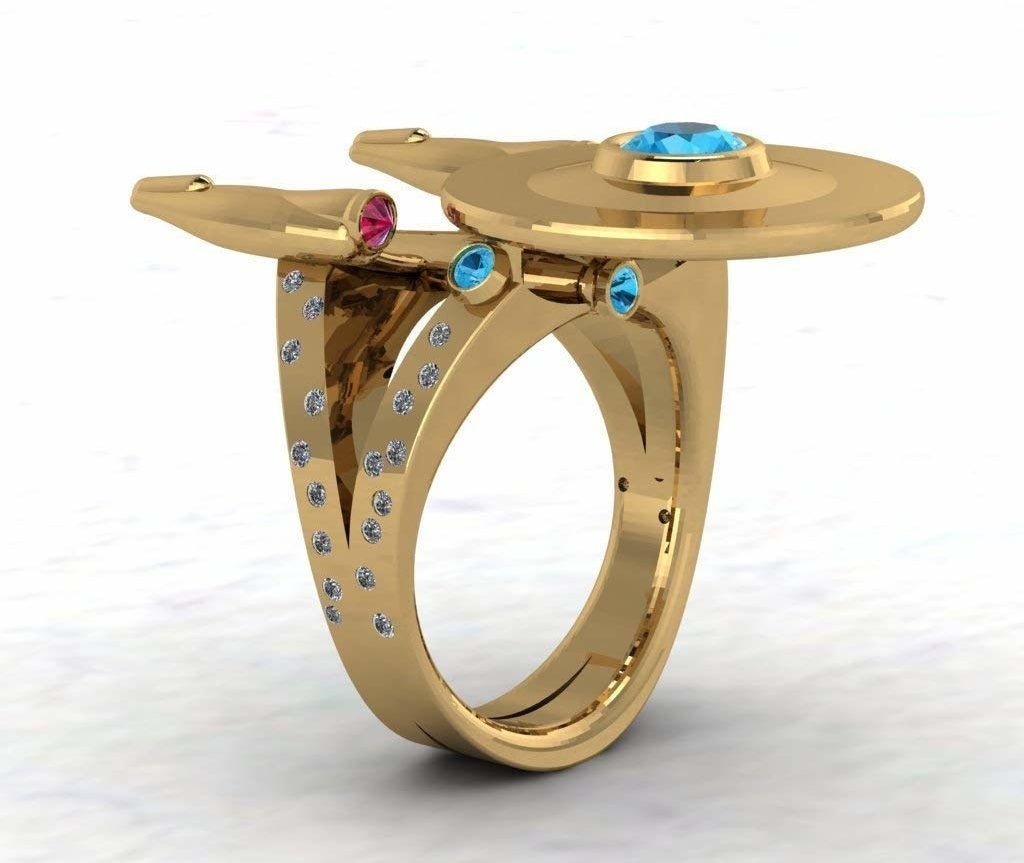 A gold ring with a diamond-encrusted band and a top shaped like Starship Enterprise from &quot;Star Trek&quot; accented with red and blue gemstones 