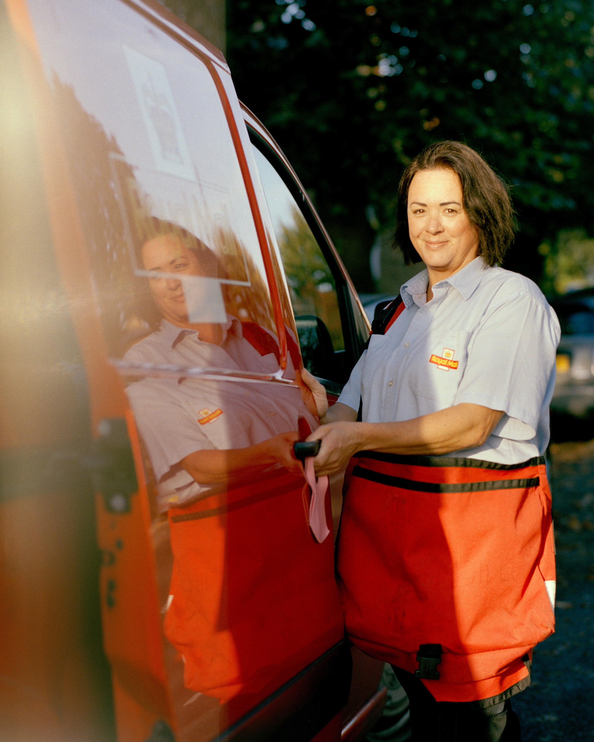 A woman postal work in the United Kingdom standing next to her truck