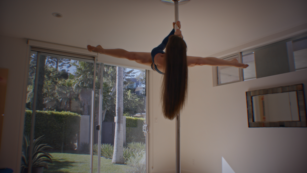 A woman does splits while high up on a pole