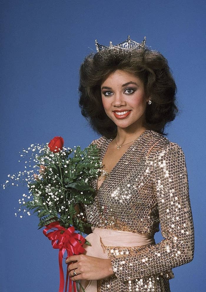 Vannessa Williams in 1983 at the Miss America Pageant wearing her tiara and a sequined dress with a sash belt while holding a rose