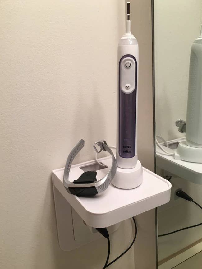 reviewer image of shelf installed over outlet and electric toothbrush on it and plugged in to outlet below