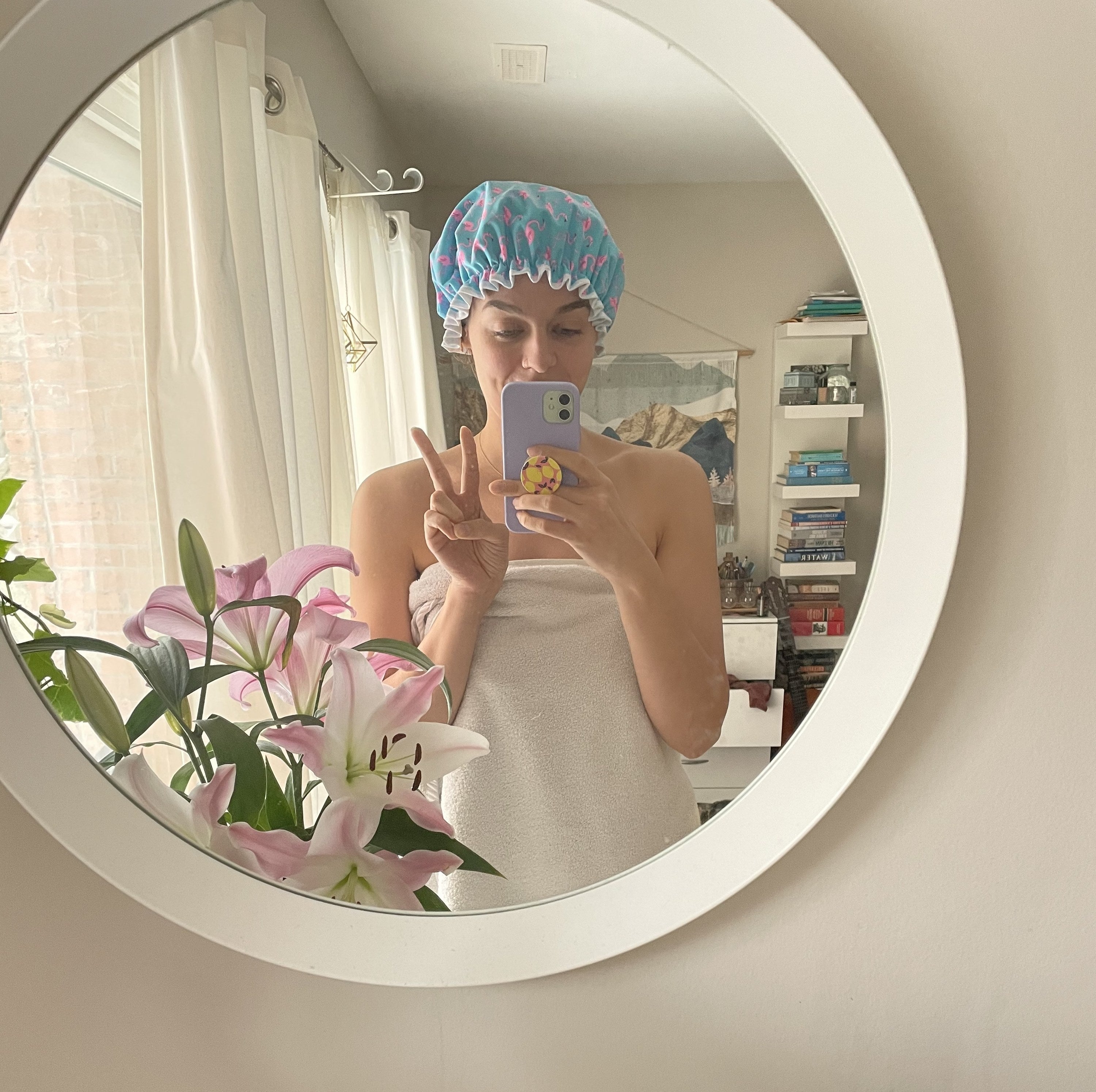 A person taking a selfie in a mirror in a towel wearing the shower cap 
