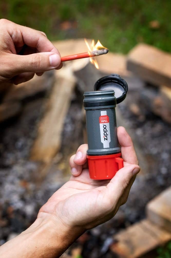 Model&#x27;s hands holding a lit match and gray and red container