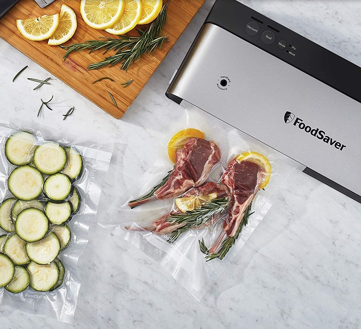 Small rectangular metal FoodSaver device on a counter next to sealed veggies and lambchops 