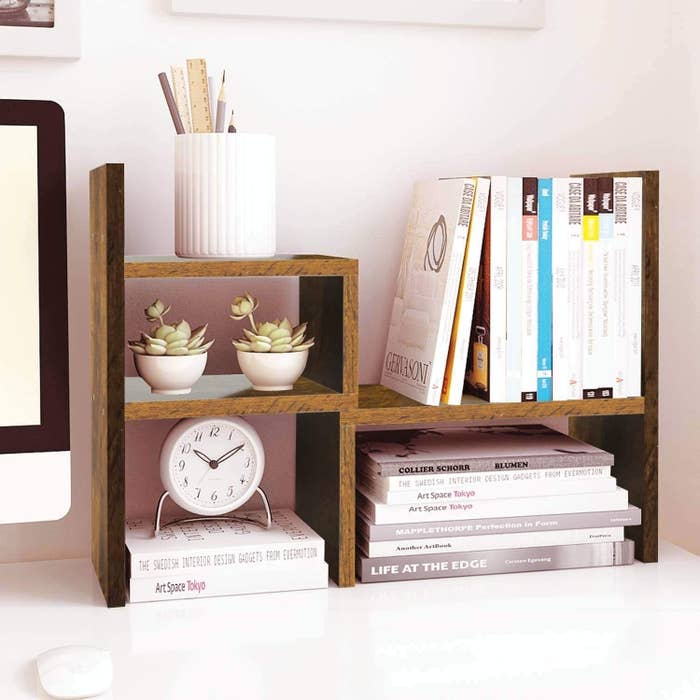 wooden shelf set holding plants, books, a clock, and a pencil cup