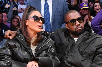 Kim Kardashian and Kanye West sit courtside at a basketball arena, each wearing fashionable outfits and sunglasses