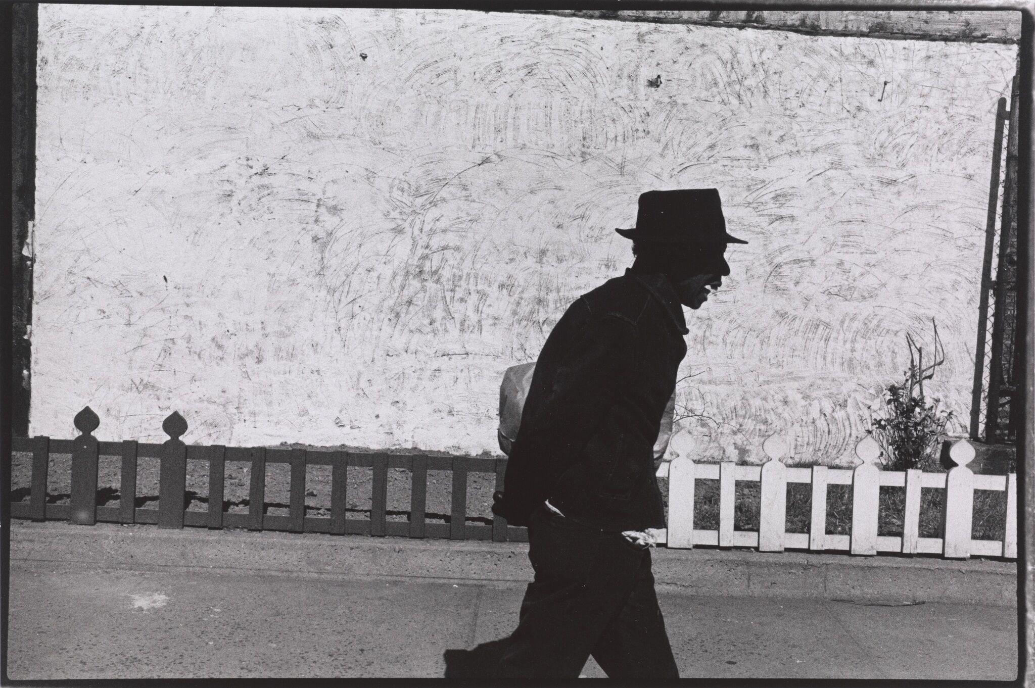 A picture of a man in black walking against a white wall