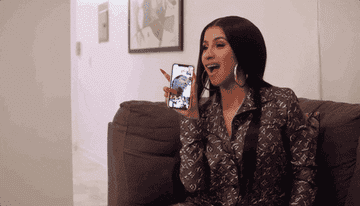 Cardi B holds up her phone while looking confused