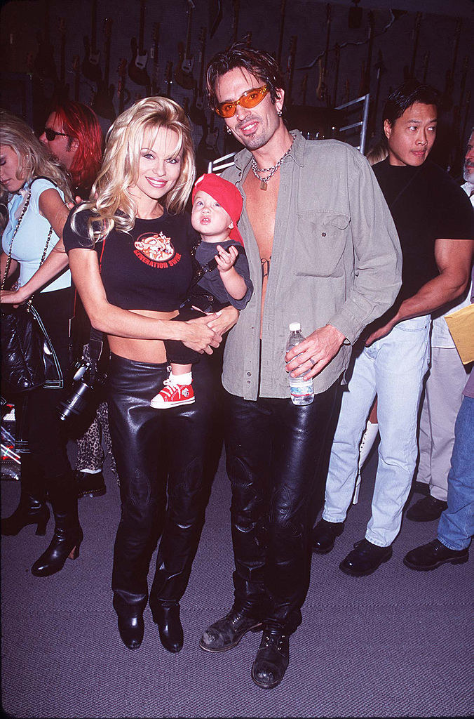 pam and tommy in leather holding up their infant son